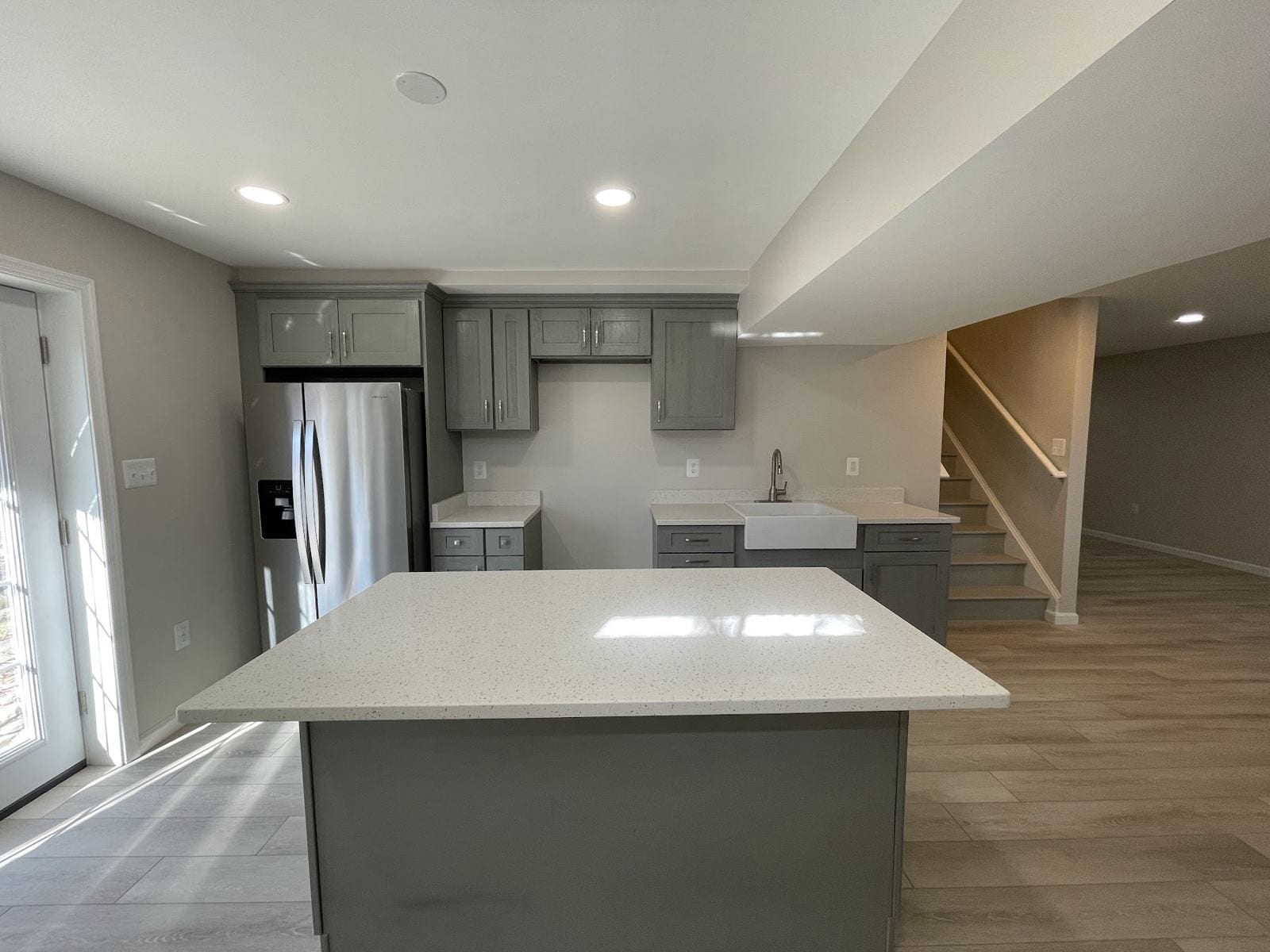 Finished basement with a gray-cabinet kitchenette, quartz island and luxury vinyl plank floor