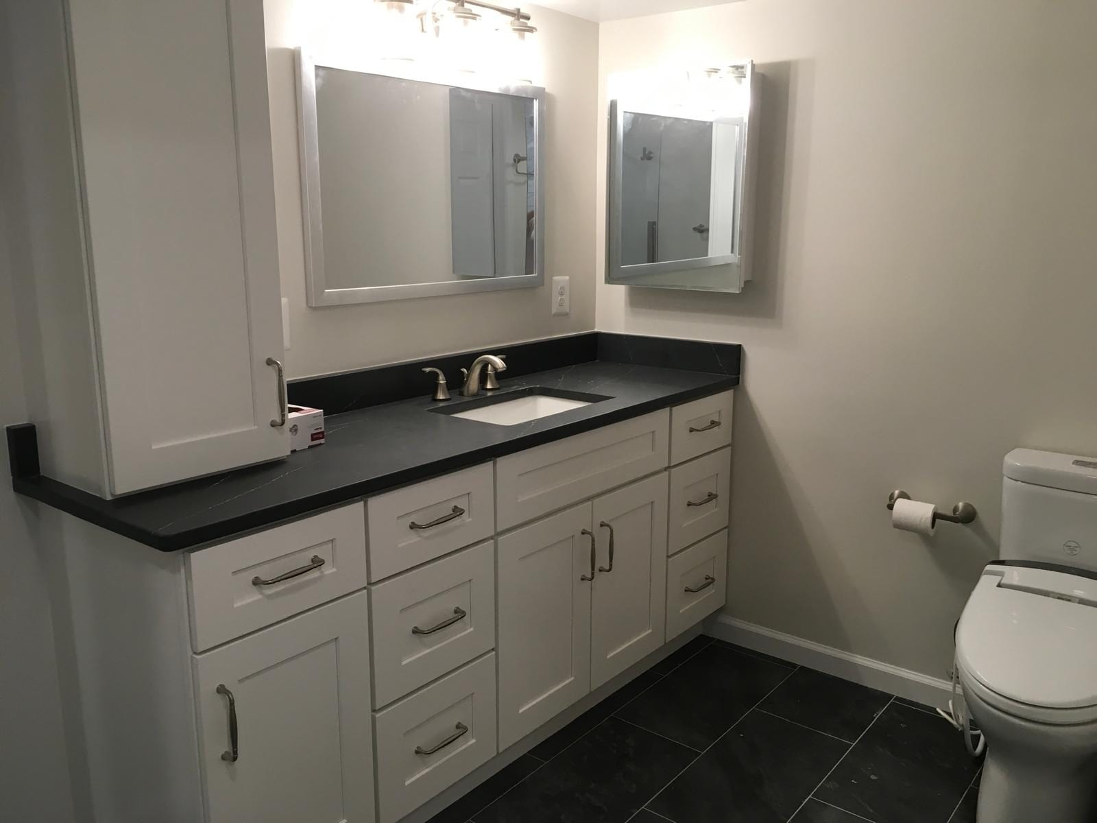 Basement bathroom with a long white vanity, black countertop, linen cabinet and slate-look floor