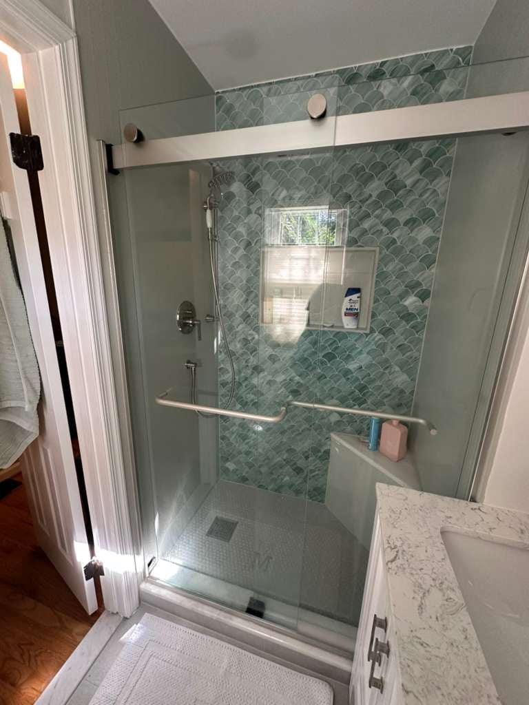Primary bathroom shower with green fish-scale tile and a sliding glass door