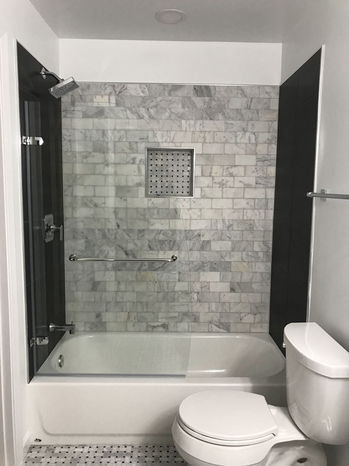 Remodeled bathroom with a marble subway-tile tub surround, recessed niche and glass panel