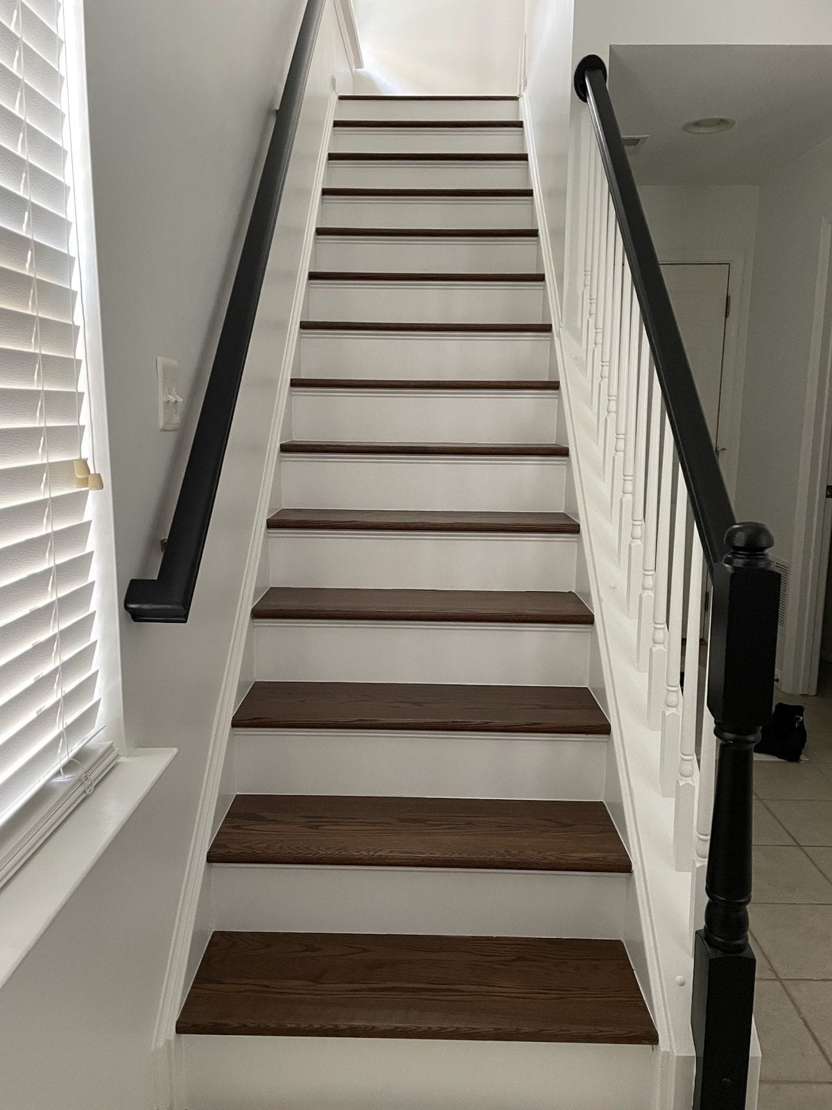 Staircase with stained wood treads, white risers and a black handrail and newel post