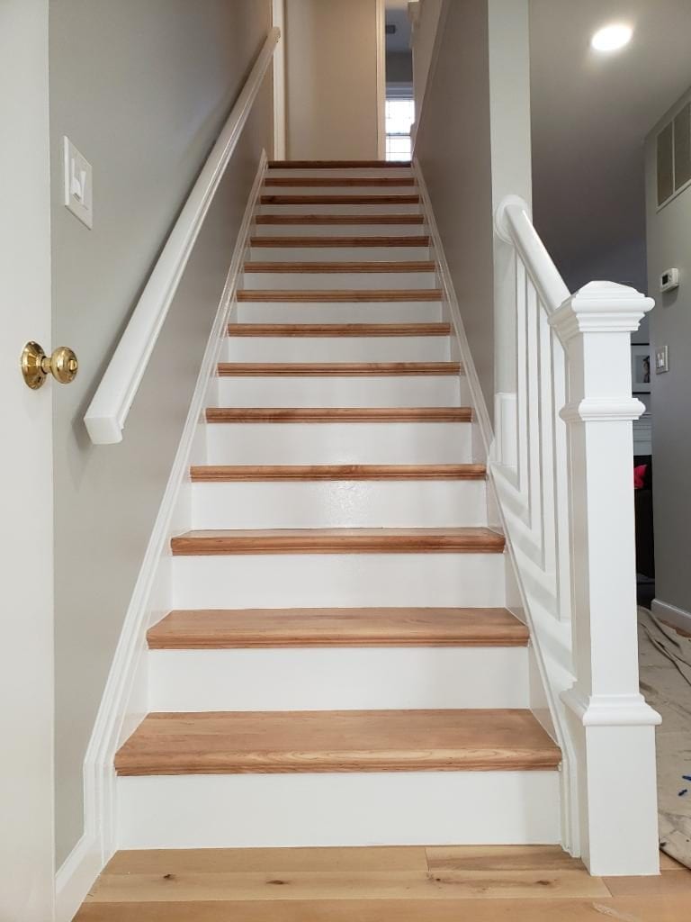 Staircase with new oak treads, white risers and a white newel post beside a wall handrail