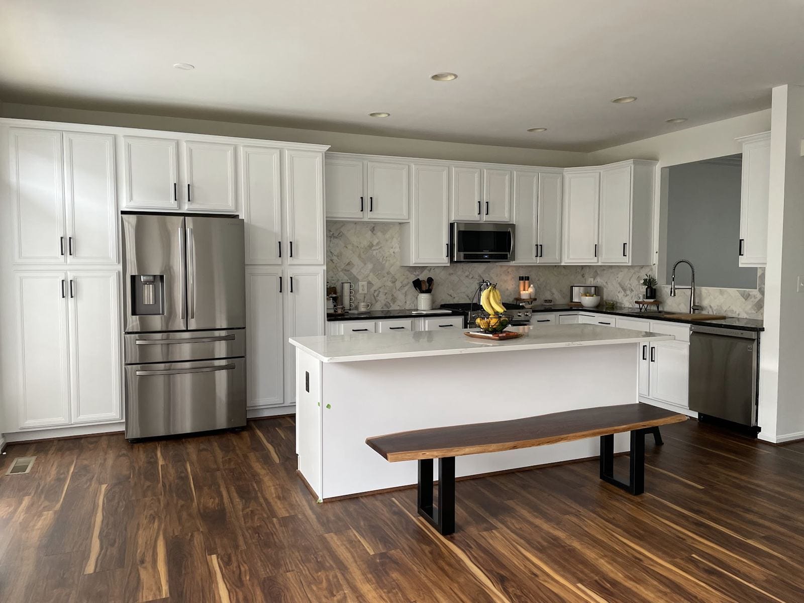 White kitchen with a quartz island, herringbone marble backsplash and new hardwood-look floor