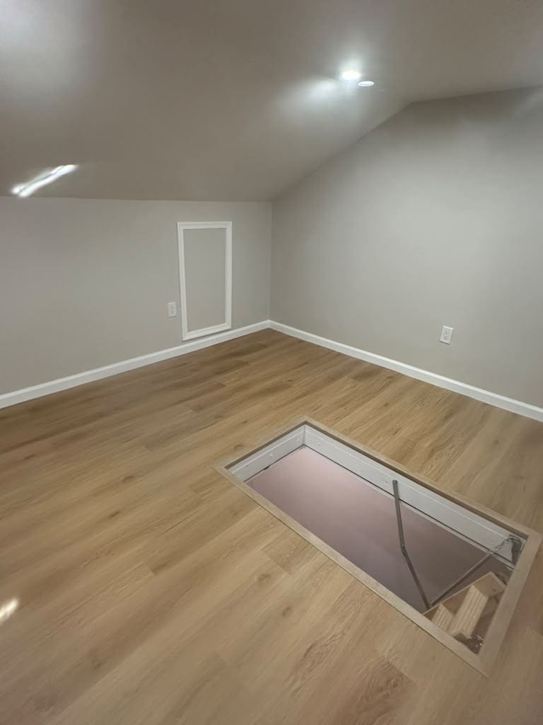 Finished attic room with vinyl plank flooring, recessed lights and a pull-down stair hatch